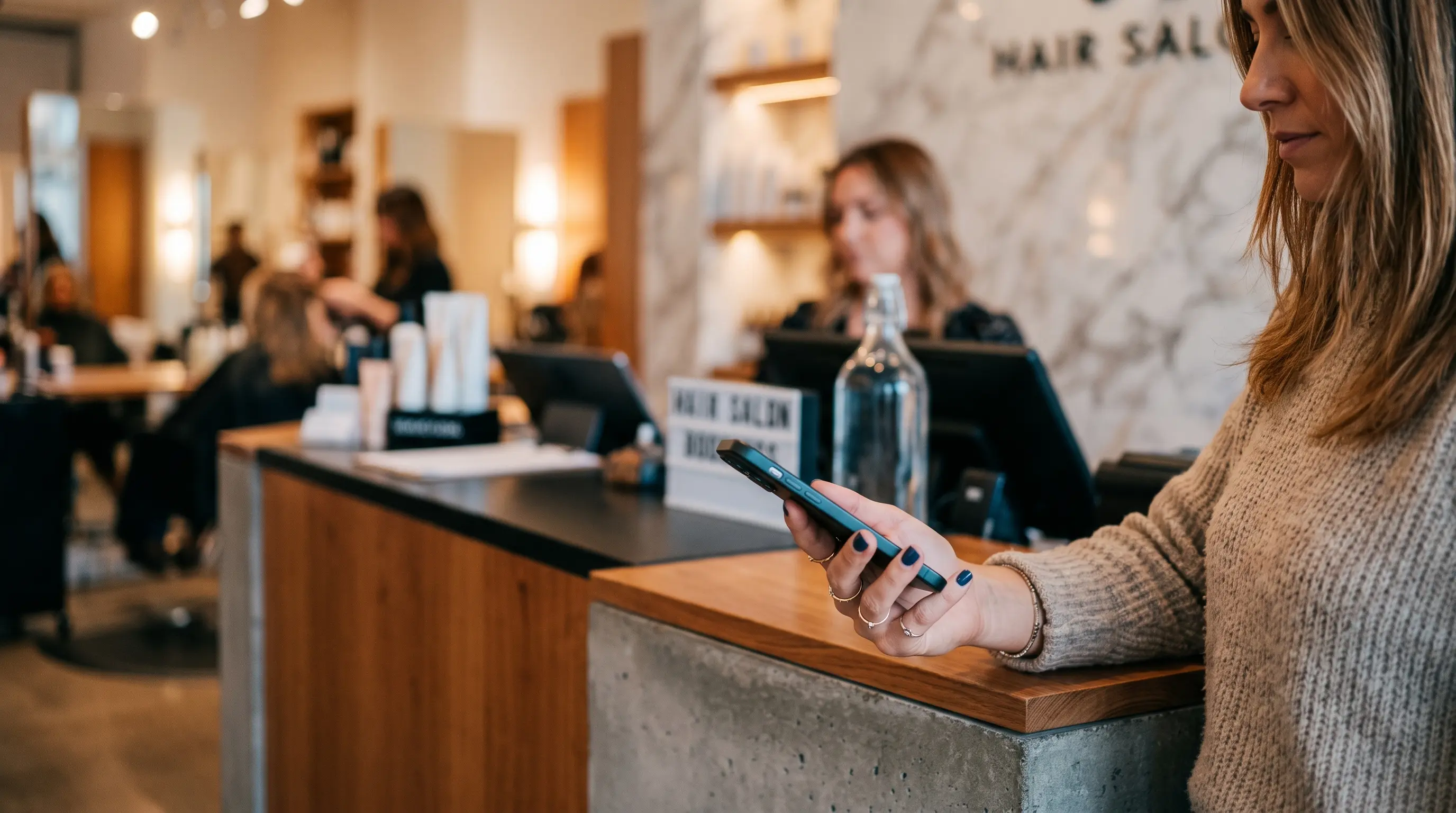 Customer's hand casually holding a phone near a modern salon reception counter, natural gesture, screen out of frame